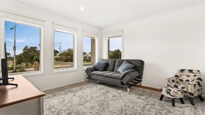 A modern living room with a grey sofa, a patterned armchair, and a desk with a computer. There are three large windows providing a view of the outside. - Bronzewing Haven in Cowes (Cowes)