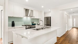 A modern kitchen with white cabinetry, a stainless steel range, and a large island with a sink. - Bronzewing Haven in Cowes (Cowes)