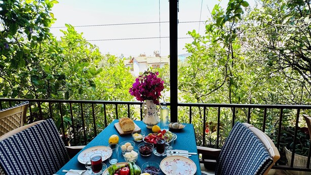 Een gedekte tafel met diverse gerechten en een bloevas op een balkon met uitzicht op groen en gebouwen.