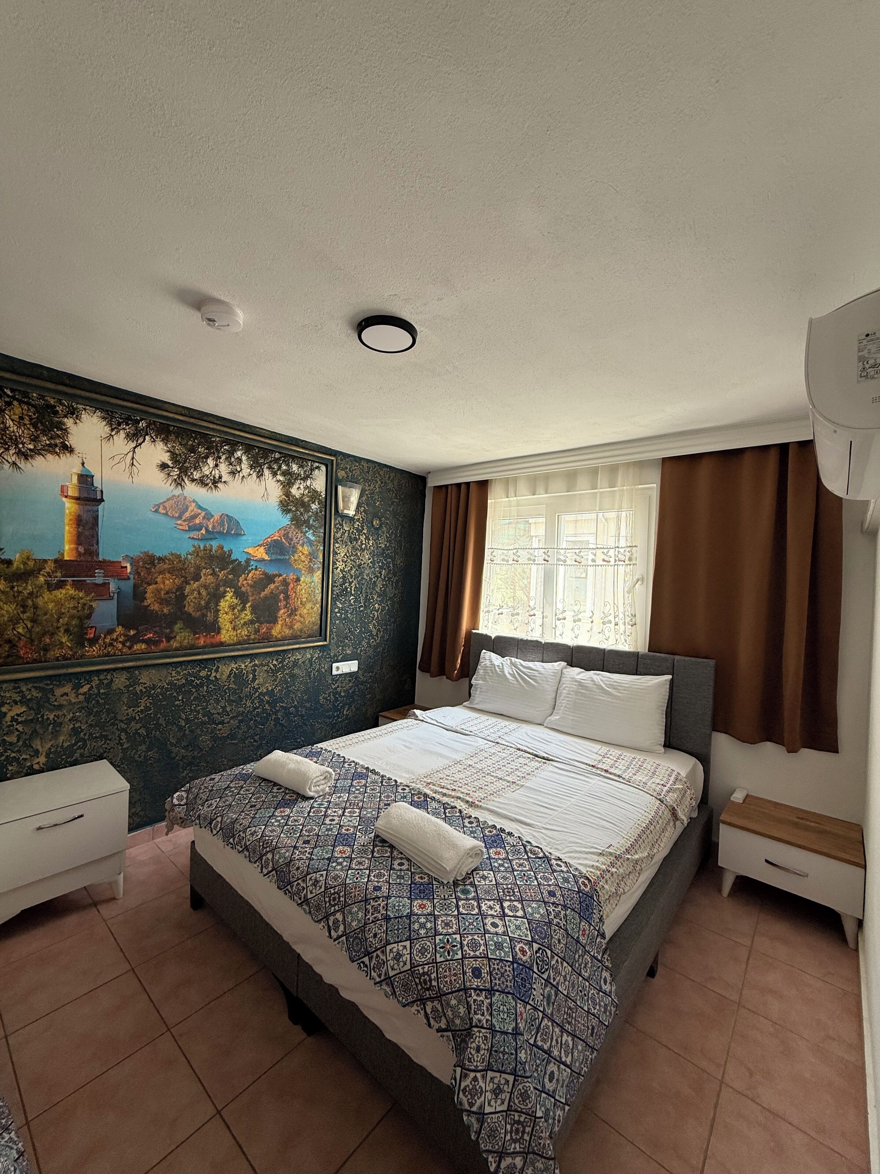 A bedroom with a bed, a nightstand, a dresser, a window with curtains, and a wall mural.