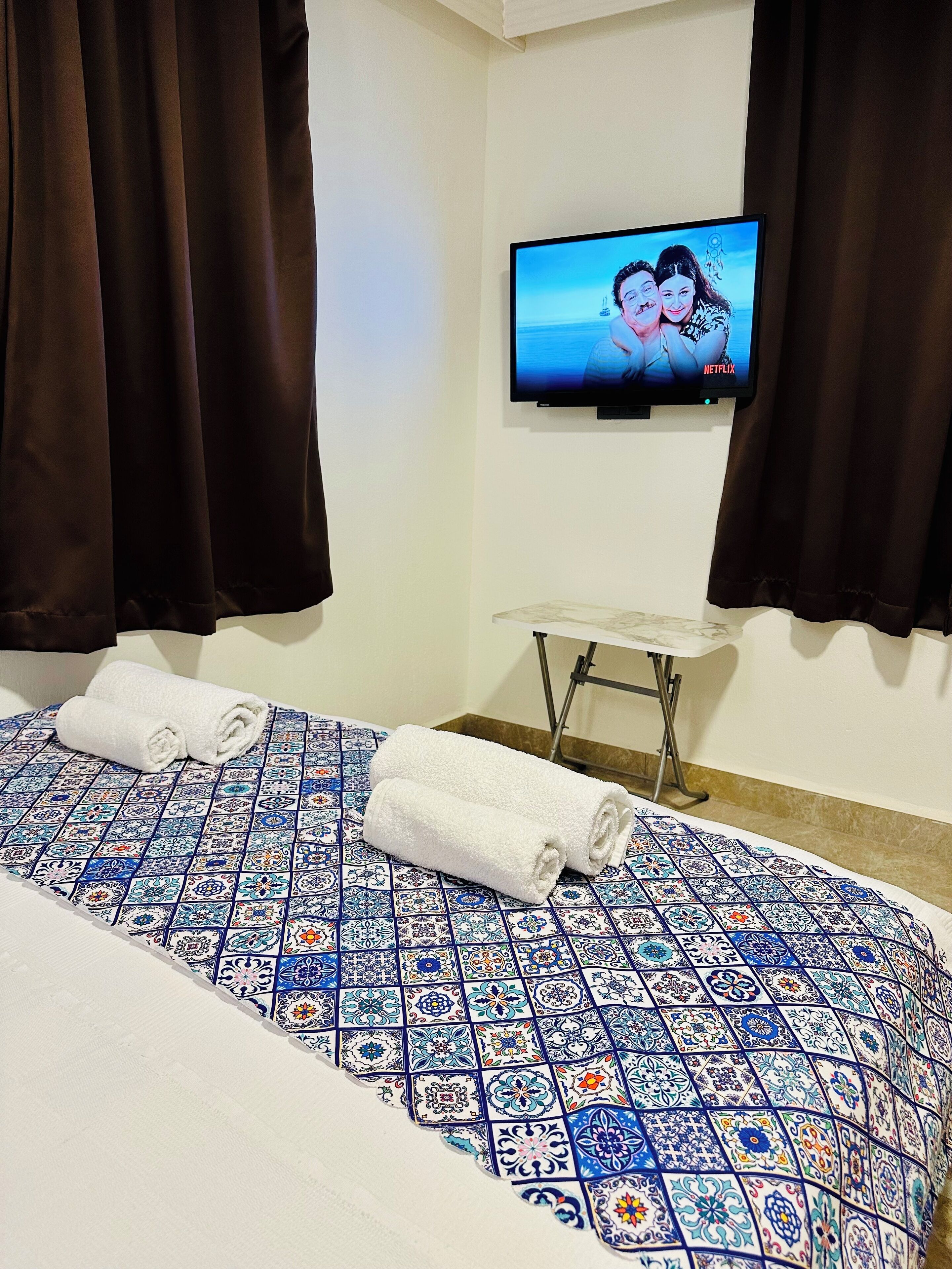A hotel room with a bed, a television mounted on the wall, and a small table.