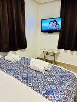 A hotel room with a bed, a television mounted on the wall, and a small table.