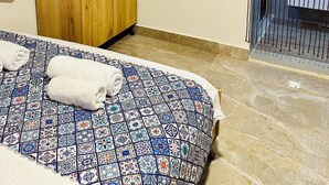 Een slaapkamer met een bed, een houten garderobe, een aan de muur bevestigde televisie en een uitzicht door een raam met een metalen traliewerk.