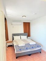 A bedroom with a bed, a nightstand, an air conditioning unit, and a window with curtains.