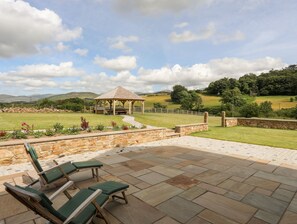 A gazebo in a landscaped garden with stone walls and a patio area with lounge chairs.