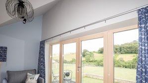 A room with a grey sofa, a ceiling fan, and large sliding glass doors leading to an outdoor area with a lawn and a fence.