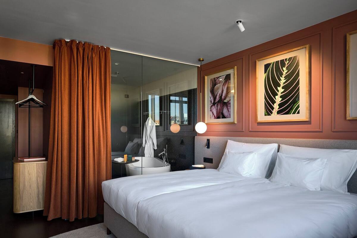 Ett modernt hotellrum med en stor säng, ett badrum med badkar och inramade konstverk på väggarna.