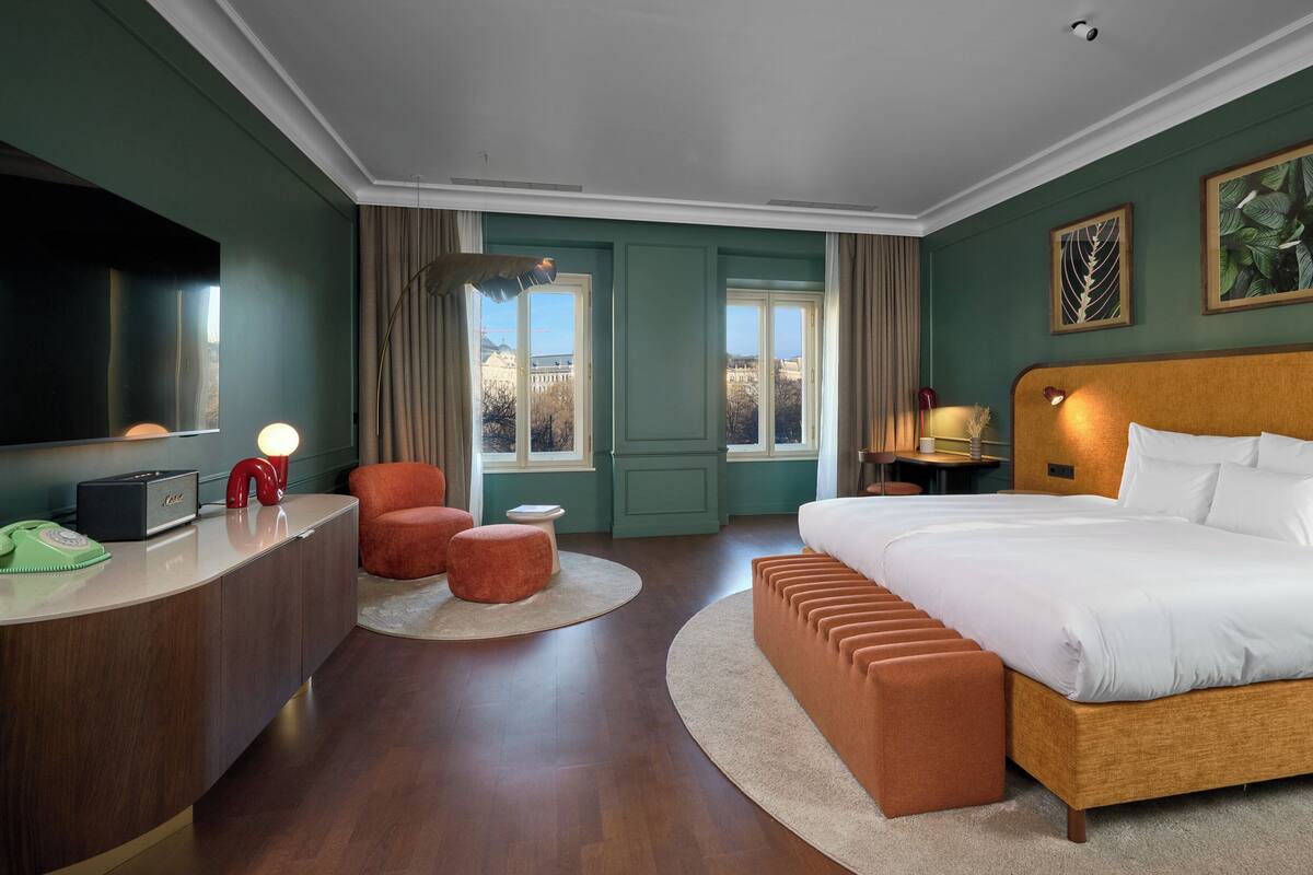 Ett hotellrum med en säng, ett skrivbord, en stol, en tv och ett fönster med utsikt.