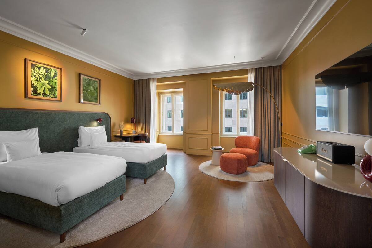 Ett hotellrum med två sängar, ett skrivbord, en stol, en spegel och ett fönster.
