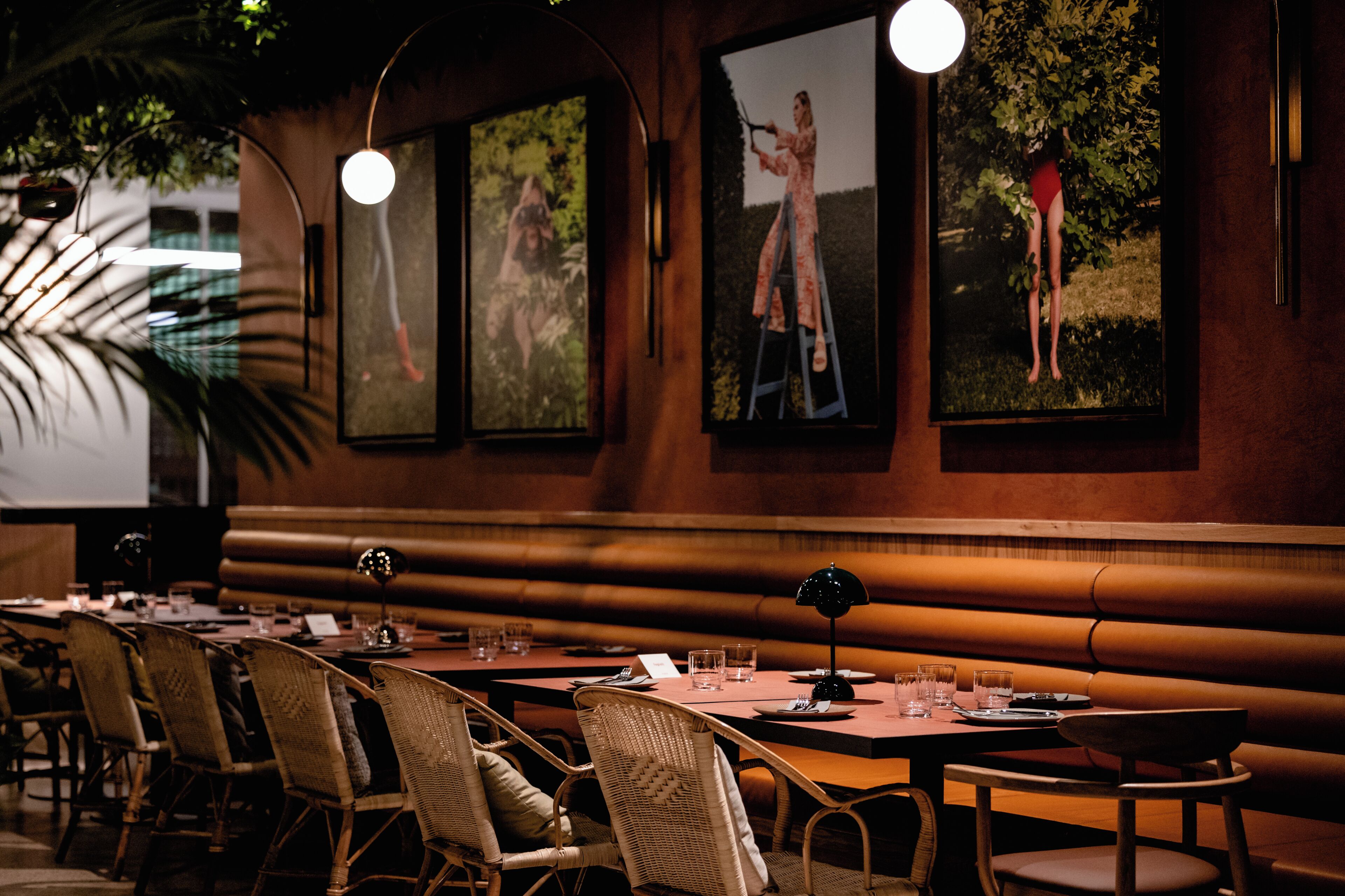 A restaurant with a long table, wicker chairs, and framed pictures on the wall.