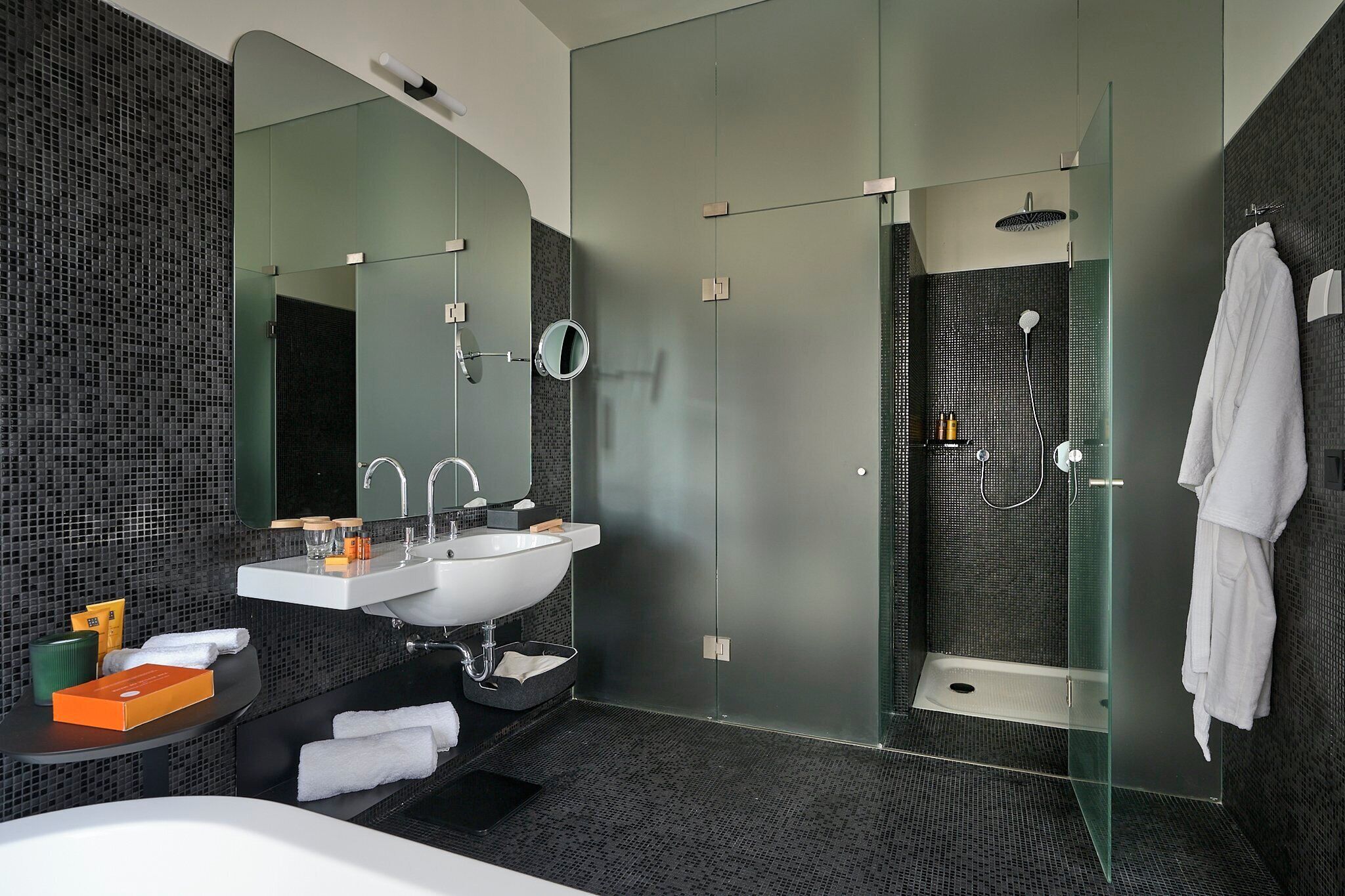 Un baño moderno con ducha de vidrio, lavamanos blanco y un espejo grande.