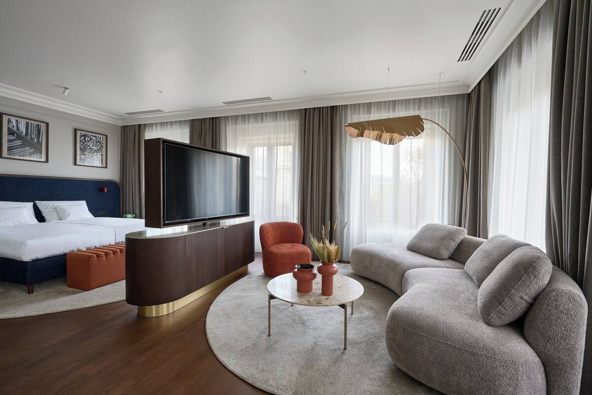Ett modernt hotellrum med en stor säng, en soffa, en tv och ett runt soffbord.