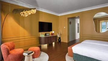A hotel room with a bed, a desk with a flat-screen TV, a large mirror, and a round rug.