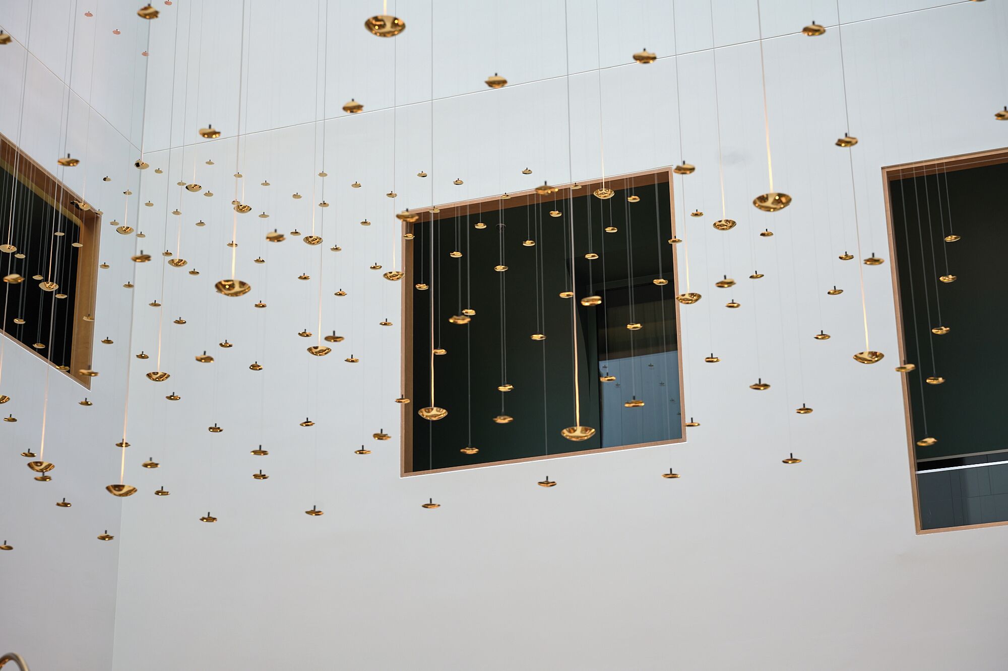 A room with multiple hanging pendant lights and two windows with dark frames.