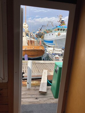 A view through a doorway of a dock with boats, a wooden bench, and a green trash bin.
