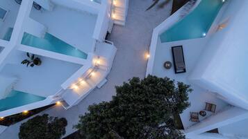 A modern hotel with multiple swimming pools, outdoor seating areas, and a large tree in the foreground.