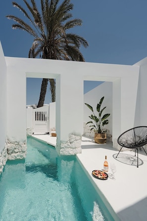 A pool area with a clear blue pool, white walls, a potted plant, a wicker chair, and a bottle of wine. - ANOME Mykonos (Mykonos)