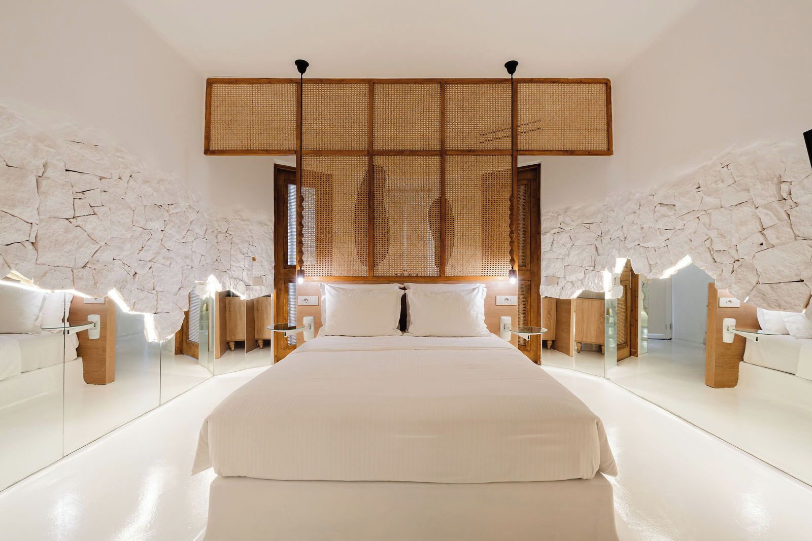 A modern bedroom with a large bed, stone walls, and a wooden partition.
