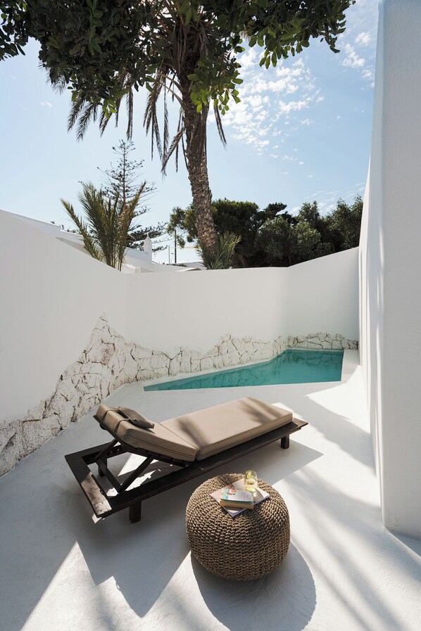 A sunlit outdoor area with a pool, a lounge chair, and a round ottoman. - ANOME Mykonos (Mykonos)