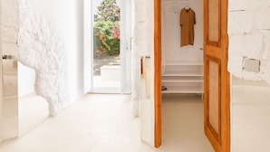 A modern interior with a white stone wall, a wooden door leading to a staircase, and a view of a garden through an open door. - ANOME Mykonos (Mykonos)