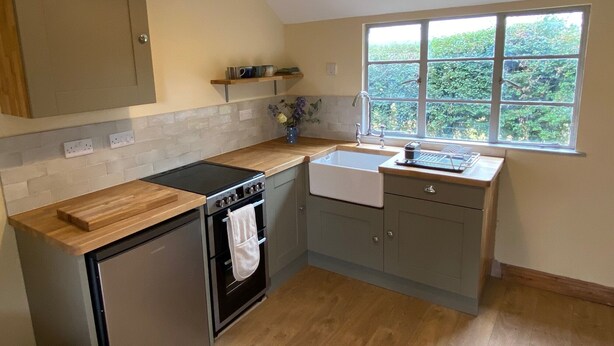 A compact kitchen with a built-in oven, a sink, and a window with a view of greenery. - Orchard Cabin Herefordshire Wye Valley (Ross-on-Wye)