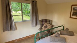 A room with a bed, a chair with a cushion, a window with curtains, and a painting on the wall. - Orchard Cabin Herefordshire Wye Valley (Ross-on-Wye)