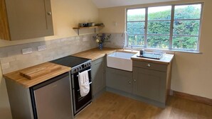 A compact kitchen with a built-in oven, a sink, and a window with a view of greenery. - Orchard Cabin Herefordshire Wye Valley (Ross-on-Wye)