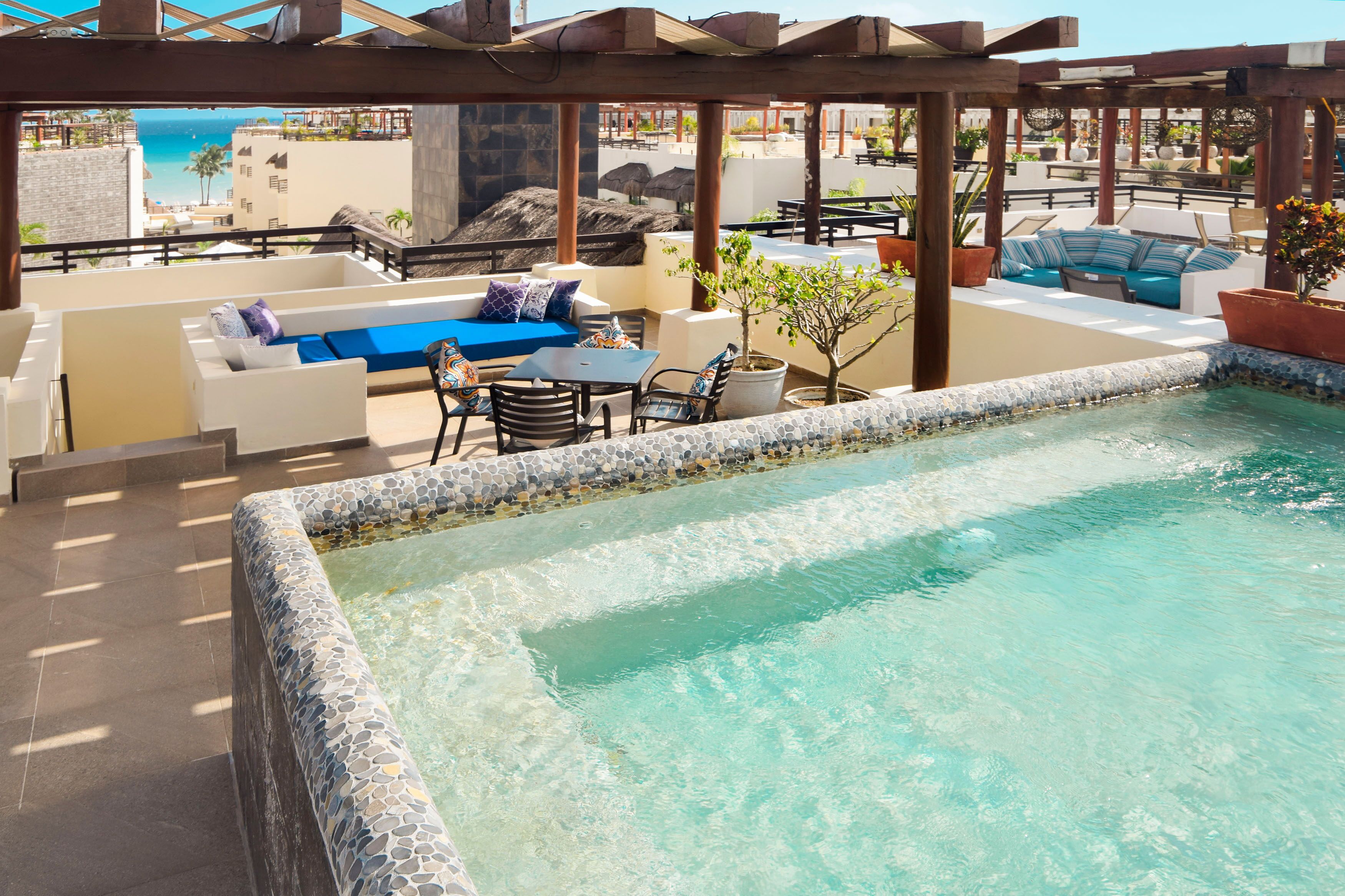 Un espace piscine aménagé sur le toit, avec un coin salon, une petite table et une vue sur l’océan.