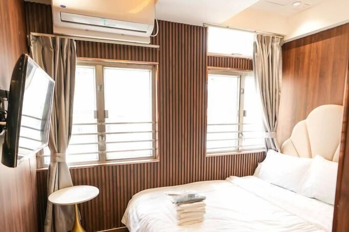A hotel room with a bed, a TV, a window, and an air conditioning unit.