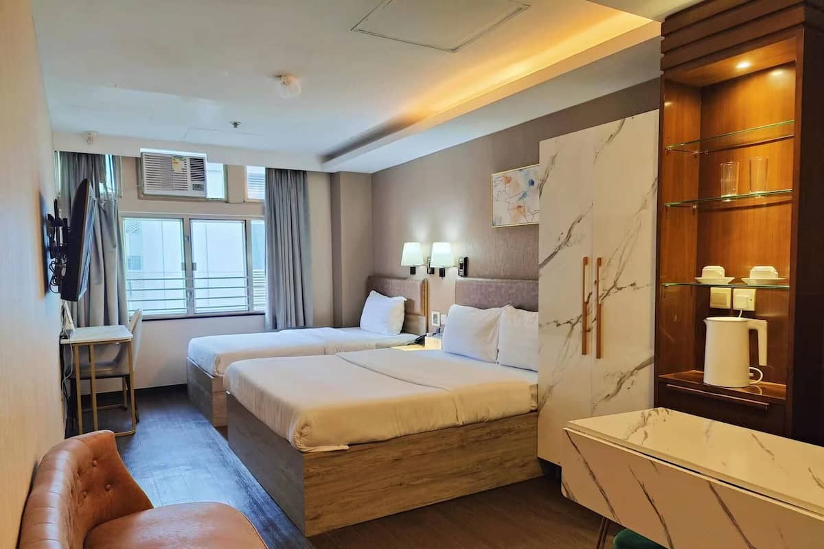 A hotel room with two beds, a desk, a chair, a small table, and a minibar.