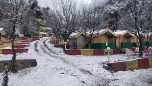 A snow-covered path leading to a row of simple, single-story buildings with green and yellow walls, likely a guesthouse or lodge.