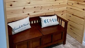 Un banc de fusta amb dos coixins, un amb la inscripció 'Beach House' i l'altre 'Beach'.