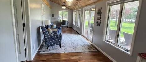 A hallway with wooden flooring, a ceiling fan, and large windows.