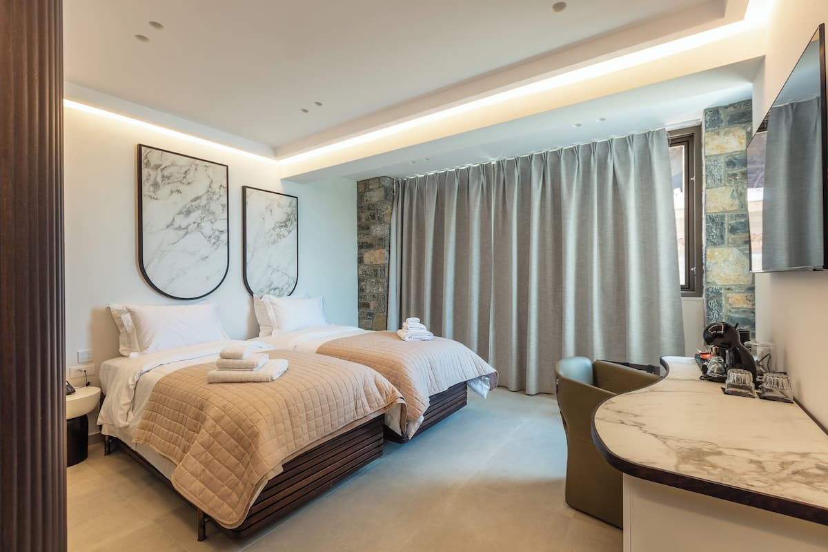 Habitació d'hotel moderna amb dos llits, un taulell de bany de marbre i una finestra gran amb cortines.