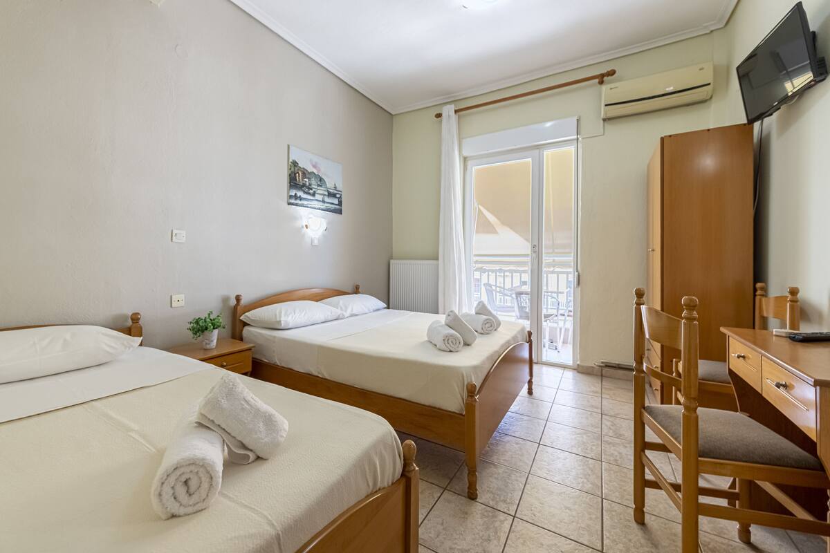 Ein Hotelzimmer mit zwei Betten, einem Schreibtisch, einem Stuhl, einem Fernseher und einem Balkon mit Blick.