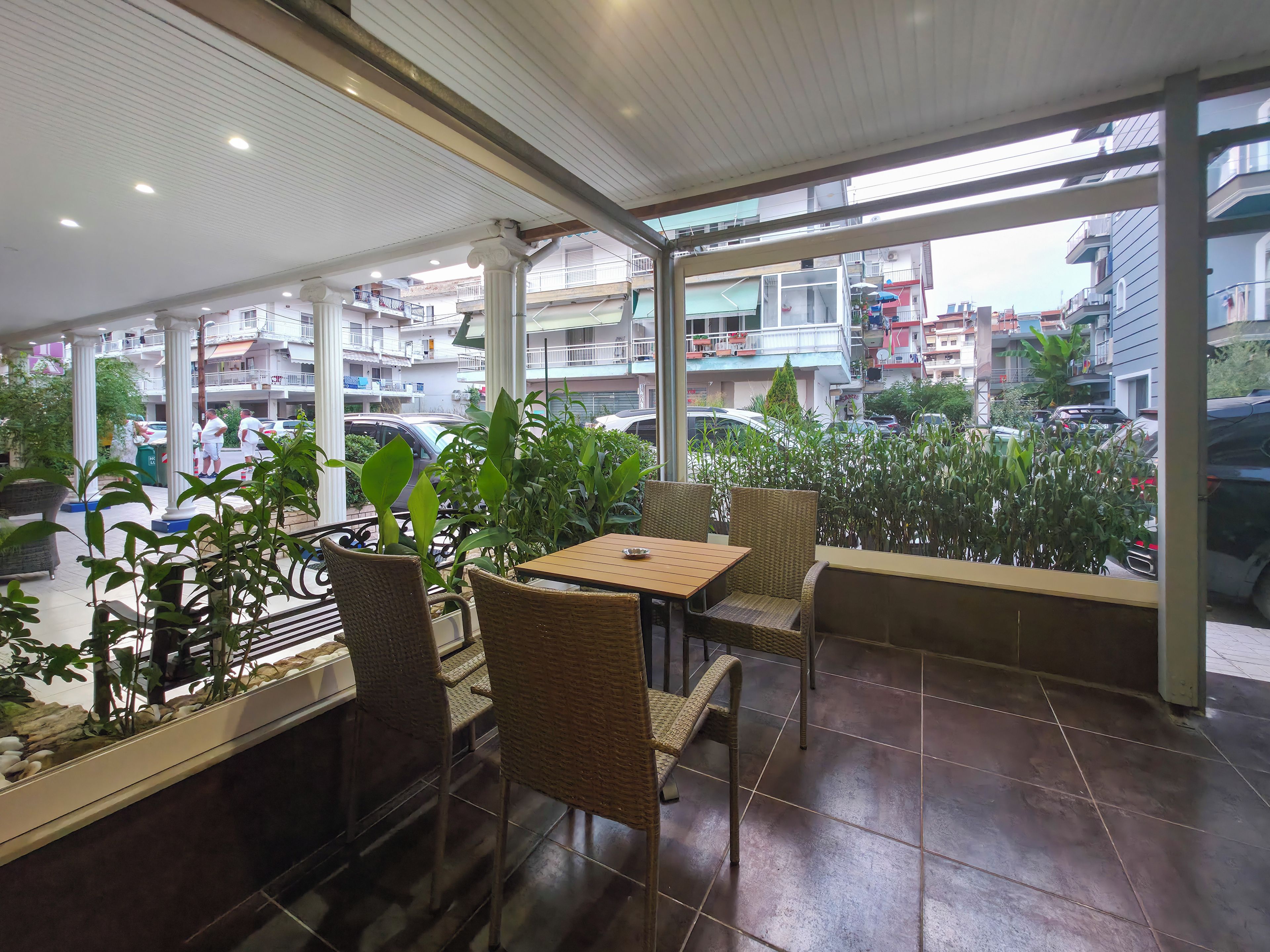 Un café con vistas a la calle, con mobiliario de mimbre y plantas en macetas.