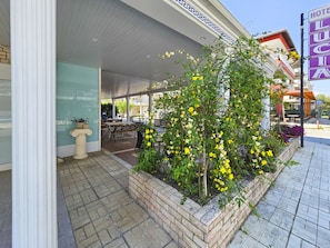 A hotel entrance with a covered outdoor seating area, a planter with yellow flowers, and a sign indicating the hotel's name. -  Lucia Hotel Paralia  (Katerini)