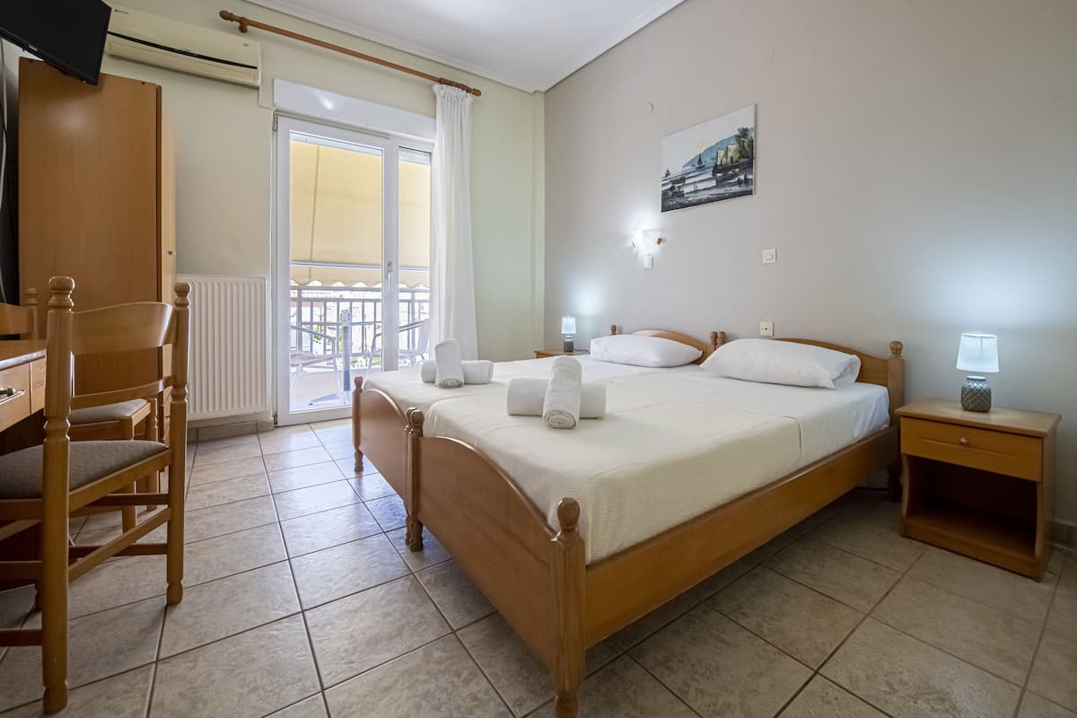 Ein Schlafzimmer mit einem hölzernen Bett, einem Schreibtisch, einem Stuhl, einem Nachttisch und Blick auf den Außenbalkon.