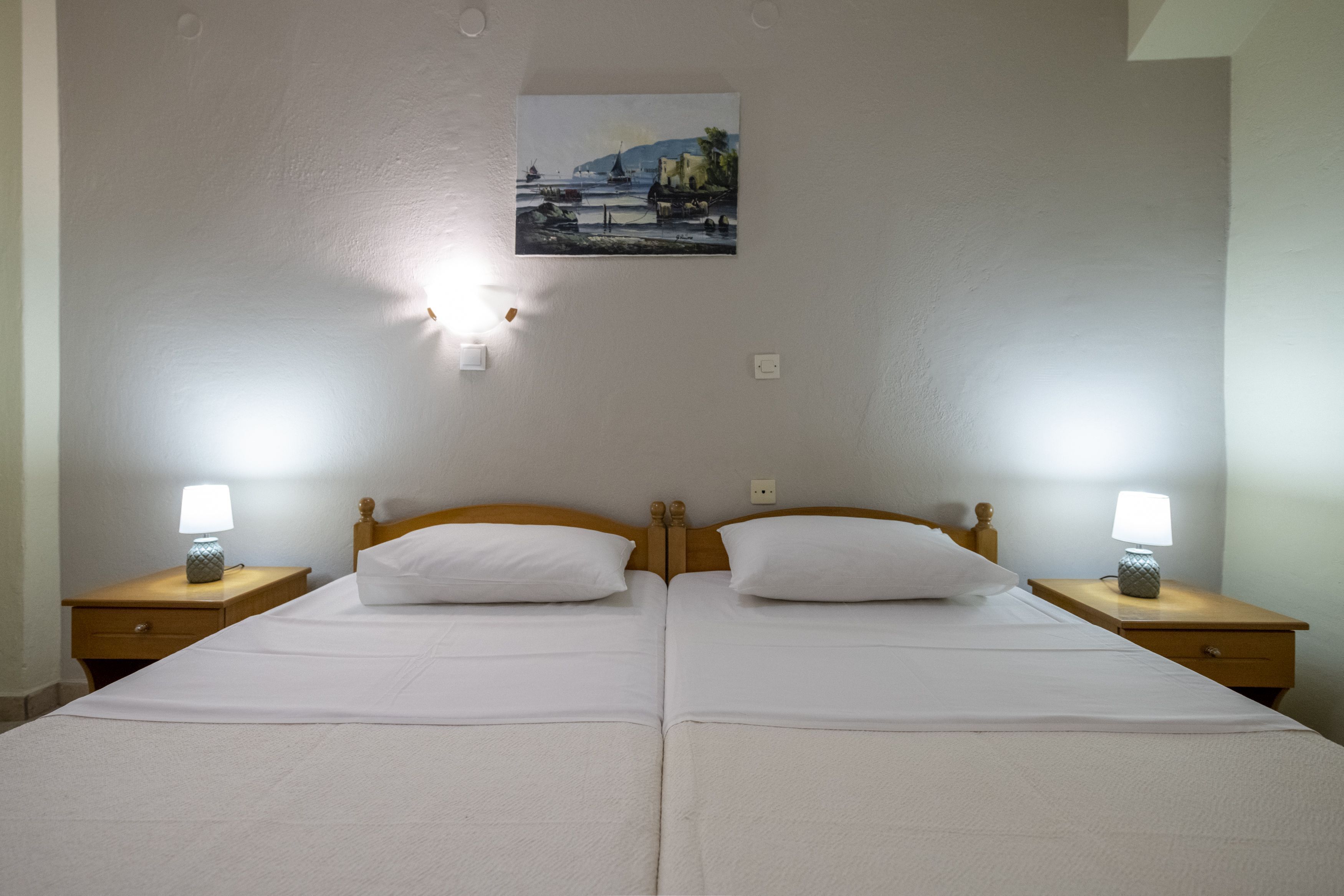 A double bed with white linens, two bedside lamps, and a painting on the wall.