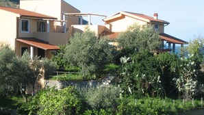 A modern two-story house with a red-tiled roof, surrounded by lush greenery and a hillside in the background. - Spisidda House - Lipari Studio - Near Gioiosa Marea (Zappardino)
