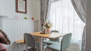Un coin repas avec une table en bois, quatre chaises grises, un vase avec des fleurs et un radiateur blanc.