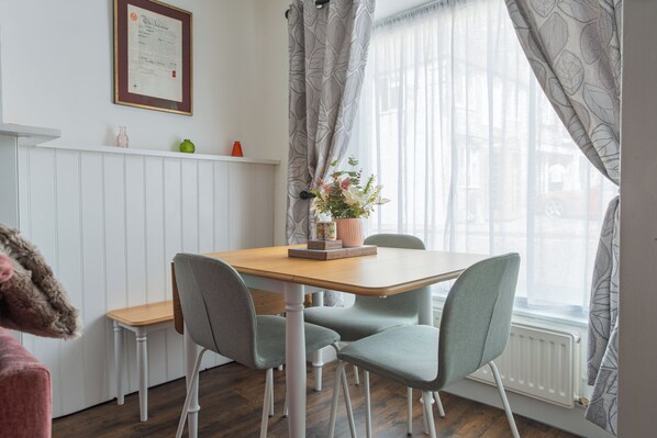 A dining area with a wooden table, four grey chairs, a vase with flowers, and a white radiator.