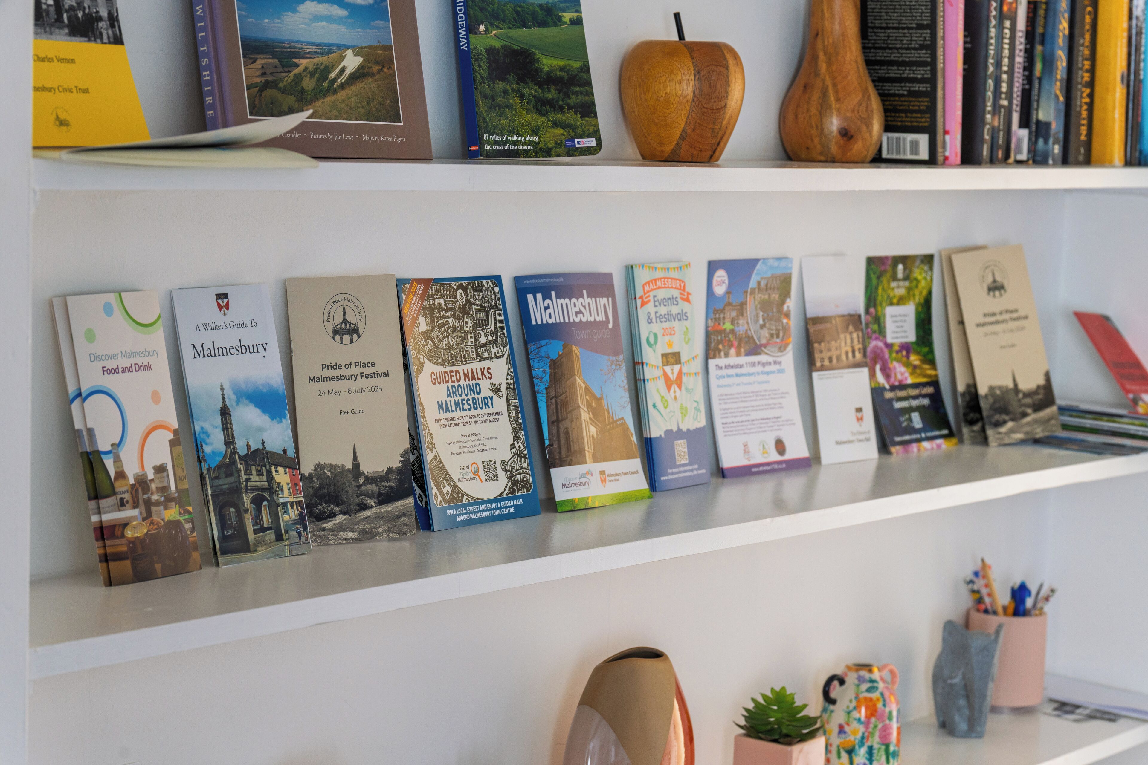 A shelf with books and decorative items, including a wooden apple and a vase.