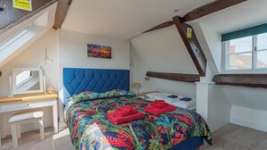 Une chambre à coucher avec une tête de lit bleue, une couvre-lit à motifs floraux colorés et une fenêtre donnant sur des immeubles.