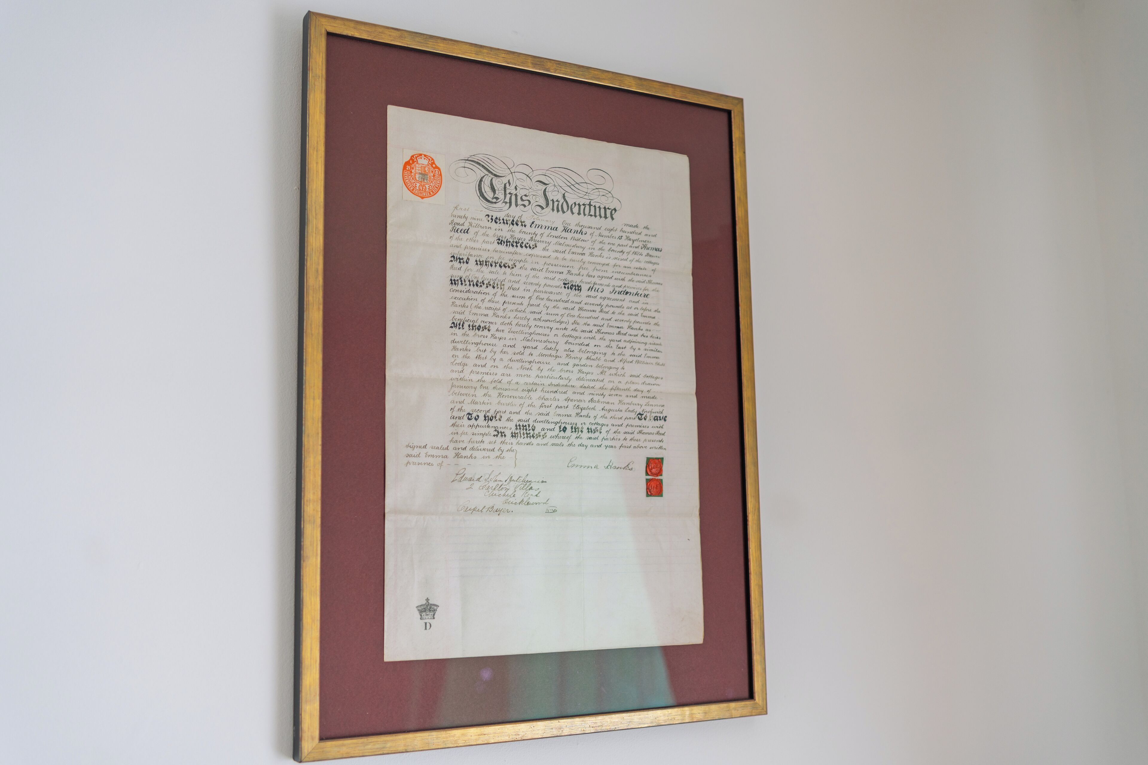 A framed document titled "This Indenture" with a wax seal and signatures at the bottom.