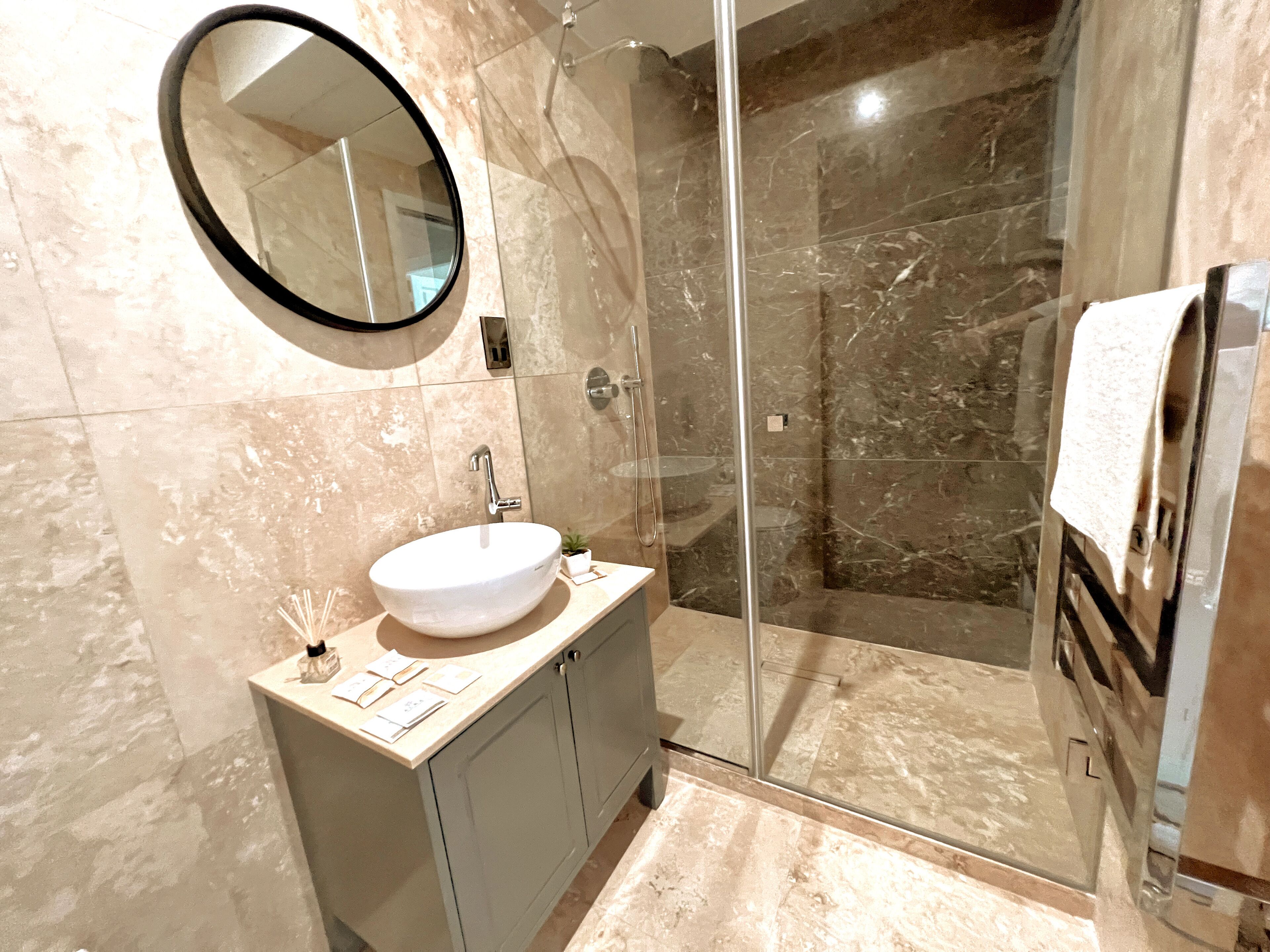 A modern bathroom with a round mirror, a sink, and a glass-enclosed shower.
