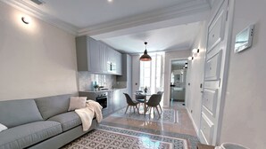A modern kitchen with grey cabinets, a dining area with a table and chairs, and a grey sofa with a throw blanket. - Work & Travel - Valletta Apartments (Valletta)