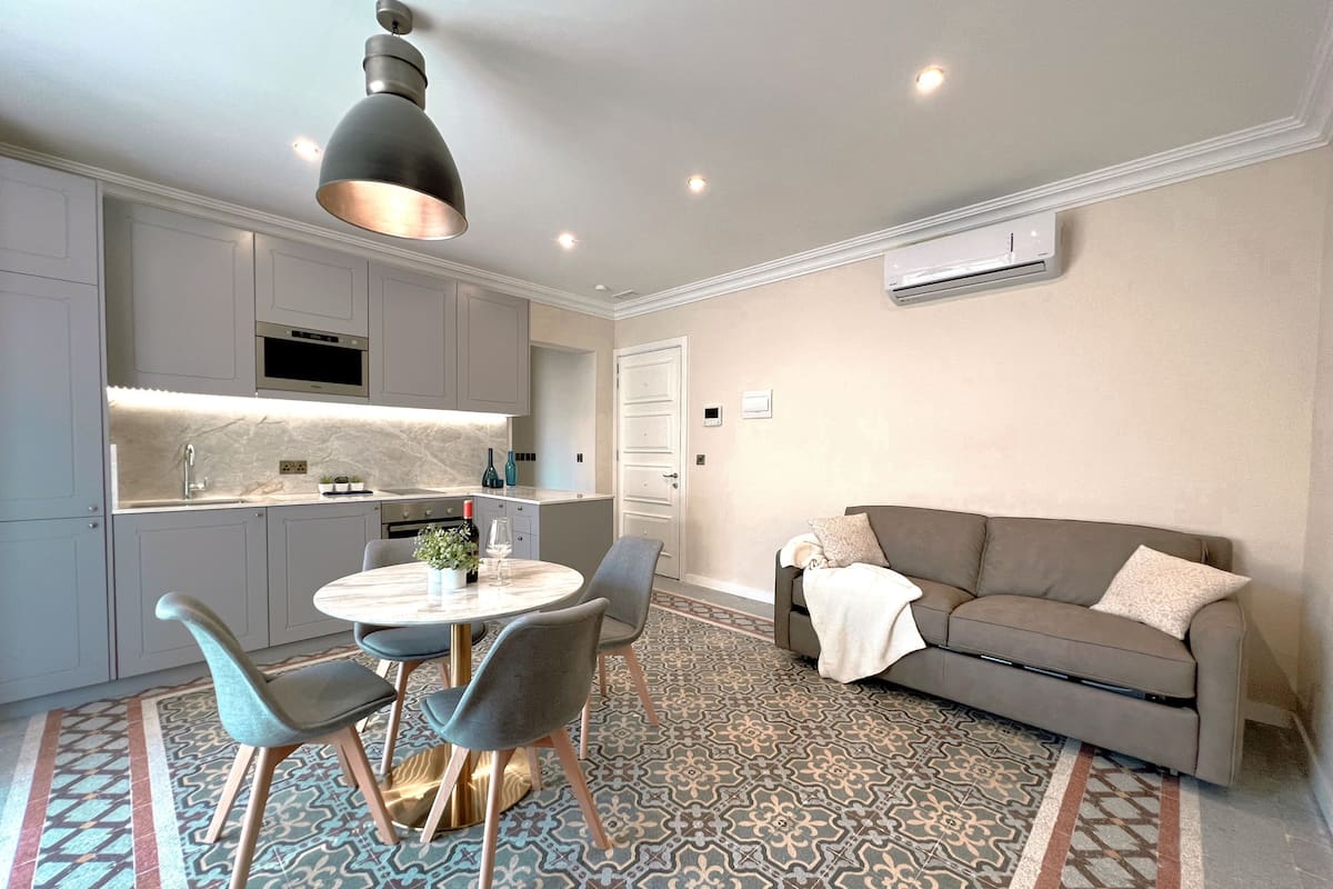A modern kitchen with white cabinets, a round dining table, and a grey sofa.