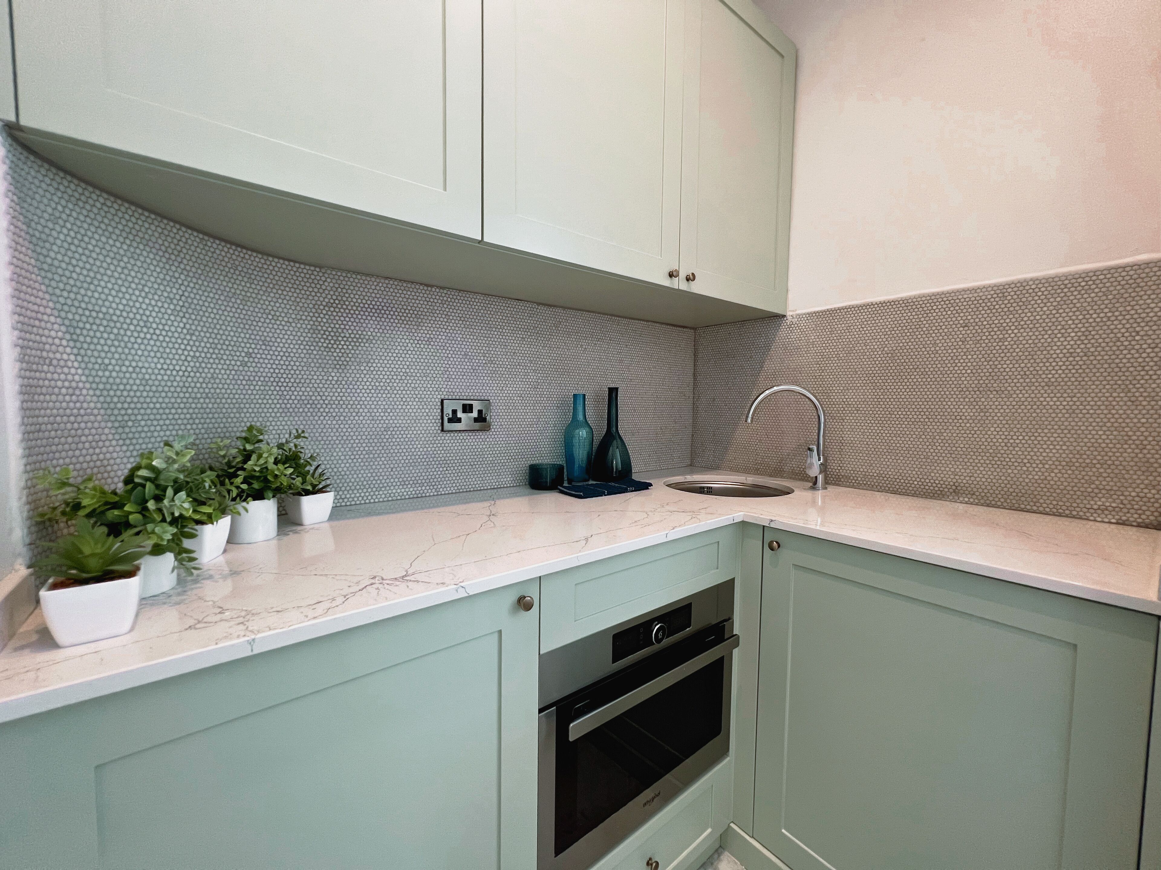 A kitchen with light green cabinets, a marble countertop, a sink, and an oven.