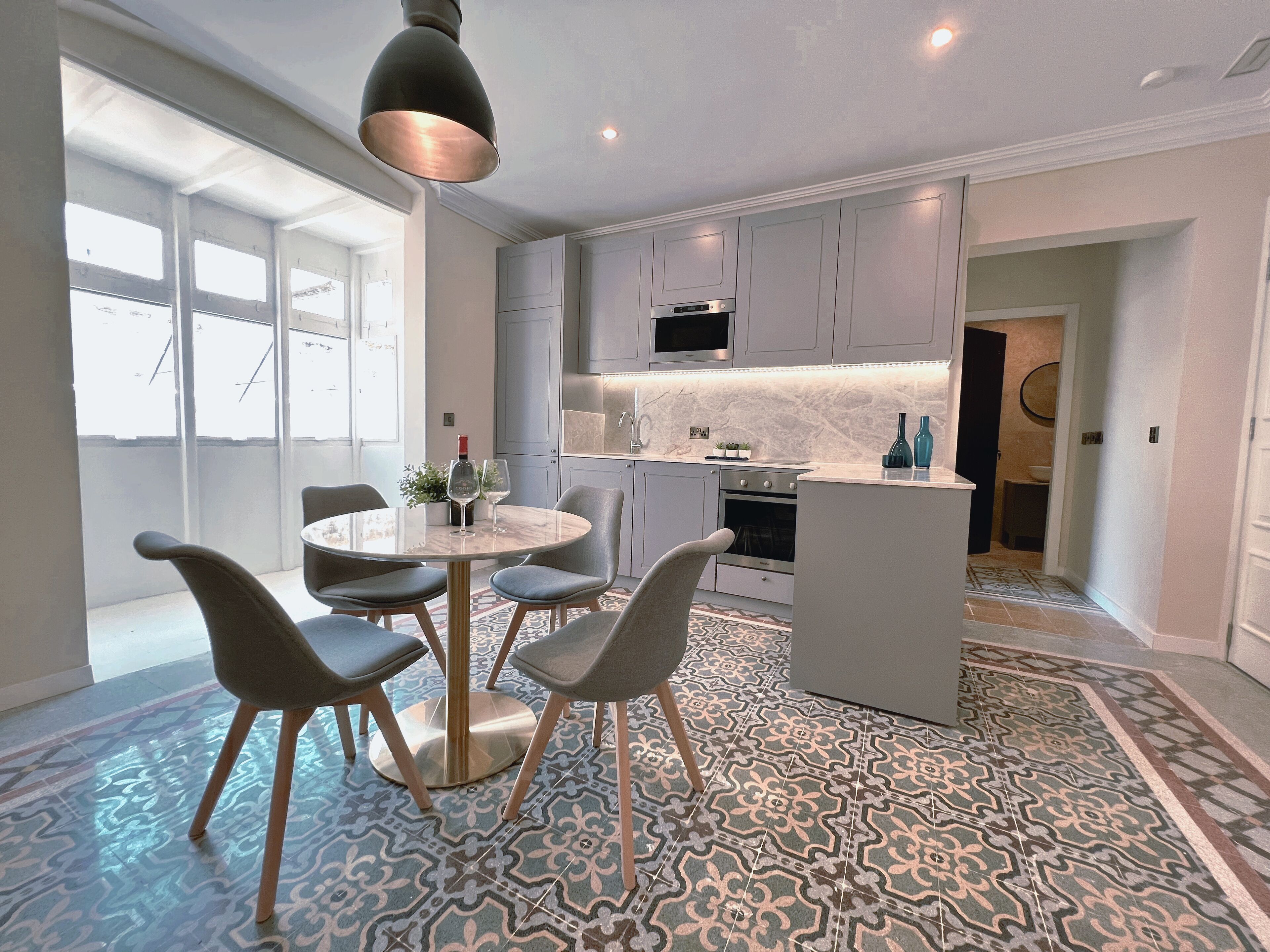 A modern kitchen with grey cabinets, a central island, and a dining area with a round table and chairs.